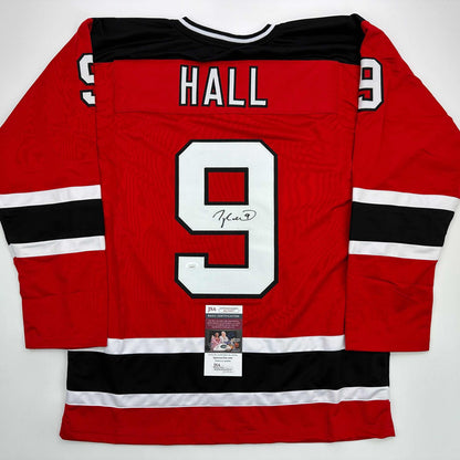Red hockey jersey with black and white stripes, number 9, "HALL" nameplate, and signature on front, displayed flat with JSA certification label visible at bottom.