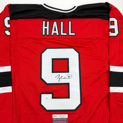Back view of red hockey jersey with "HALL" and number 9 in white, signed in black marker, with JSA authentication label at bottom.