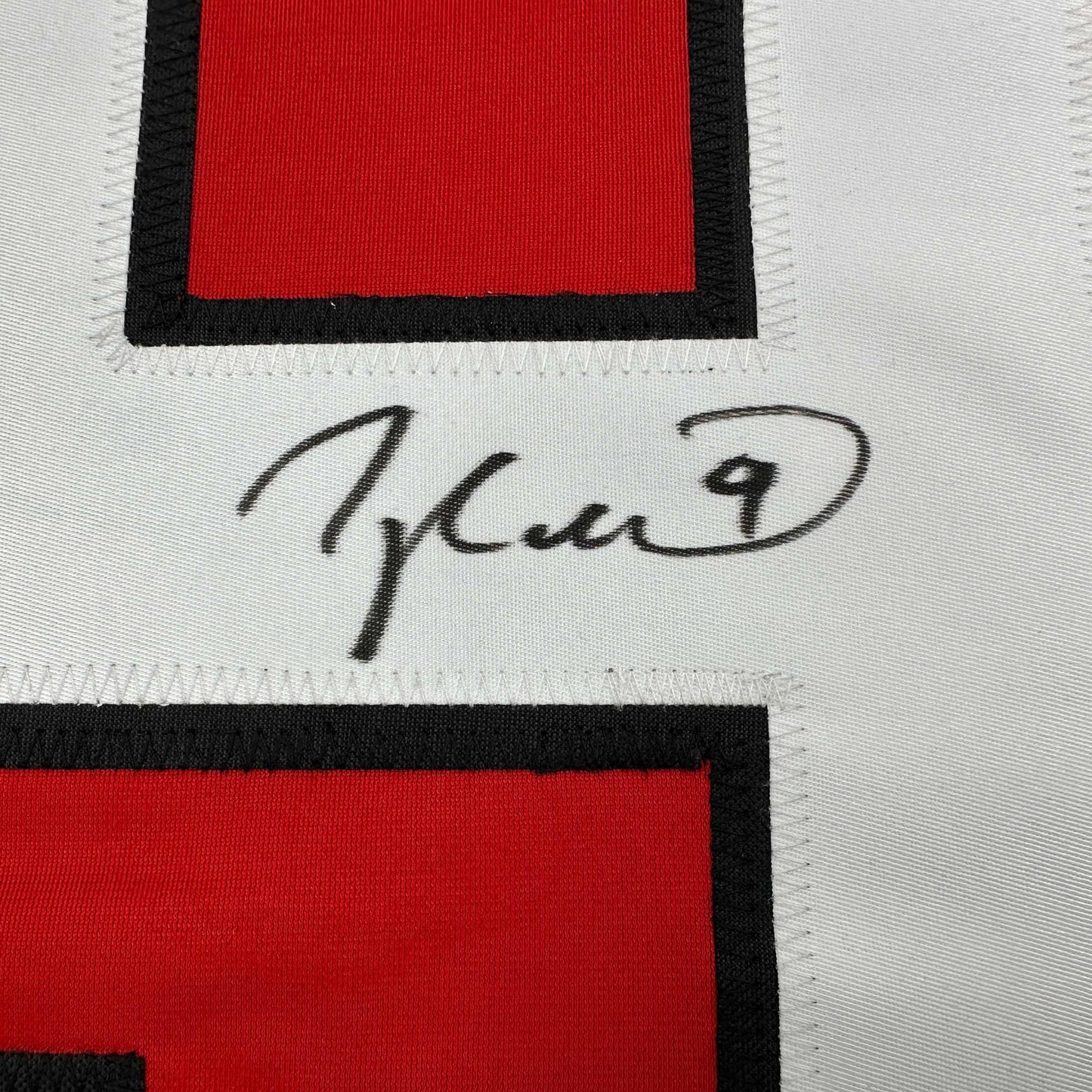 Close-up of handwritten signature on white fabric between red and black striped sections of hockey jersey.