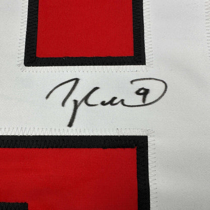 Close-up of handwritten signature on white fabric between red and black striped sections of hockey jersey.