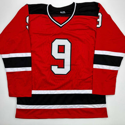 Red hockey jersey with black and white horizontal stripes, number 9 on chest, displayed flat on white background.