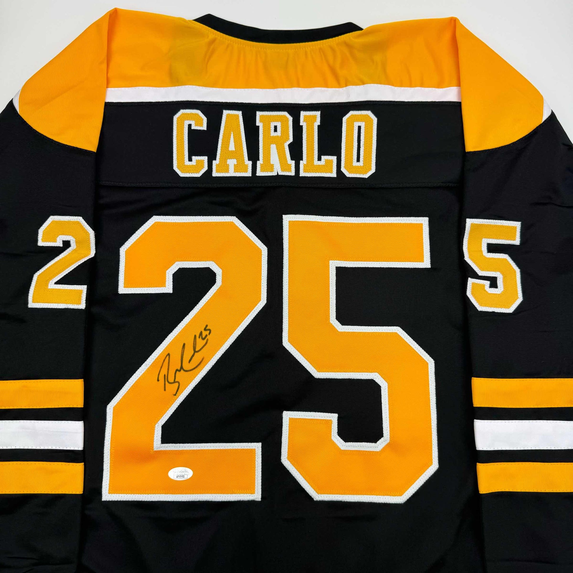 Back view of black and gold Boston Bruins hockey jersey with "CARLO" and number 25 embroidered in yellow and white, signed in black marker.