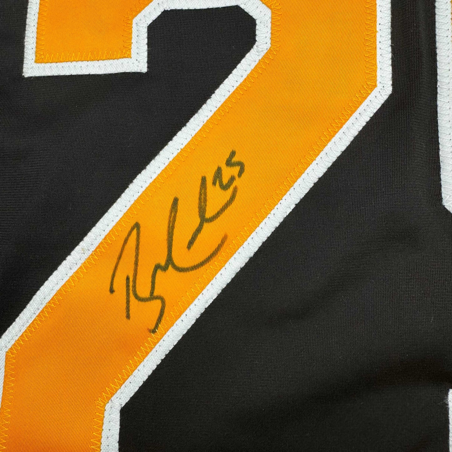 Close-up of signed orange and black hockey jersey stripe with handwritten autograph on yellow fabric.