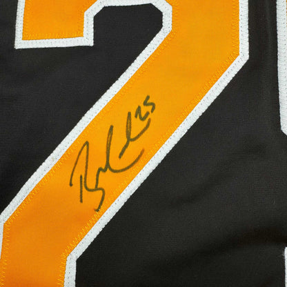 Close-up of signed orange and black hockey jersey stripe with handwritten autograph on yellow fabric.