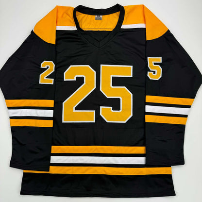 Black and gold hockey jersey with number 25 displayed flat against white background, front view showing V-neck collar and striped sleeves.