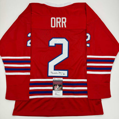 Red hockey jersey with "ORR" and number 2 displayed, showing back view with JSA authentication certificate attached.