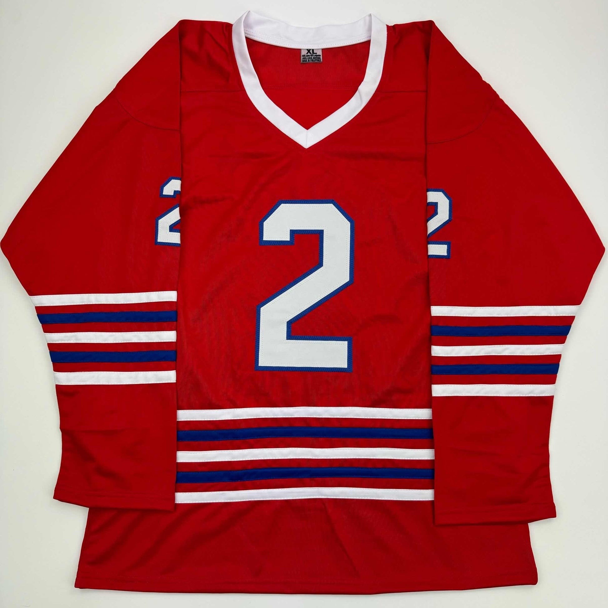 Red hockey jersey with white v-neck collar, large white number 2 with blue outline, red-white-blue striped sleeves and waistband, displayed flat on white background.