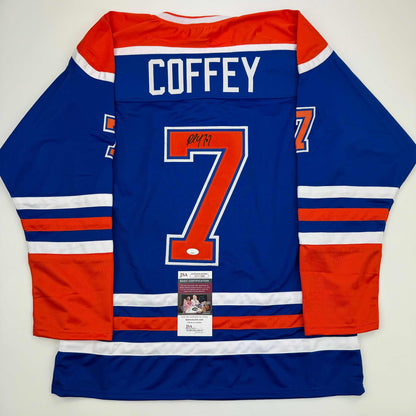 Back view of signed blue Edmonton Oilers jersey number 7 with "COFFEY" nameplate and JSA authentication certificate visible.