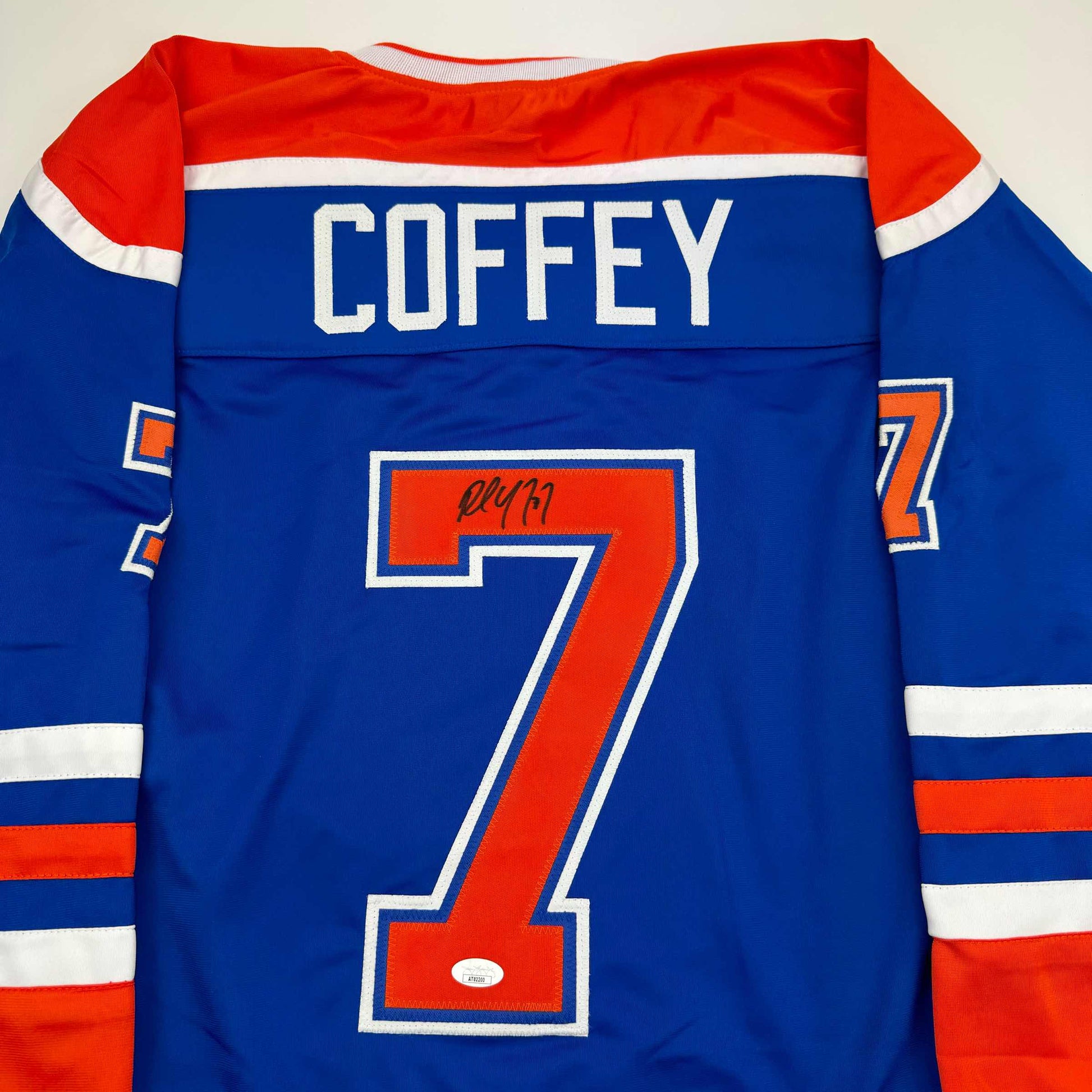 Back view of blue Edmonton Oilers hockey jersey with "COFFEY" nameplate and number 7 in red, autographed in black marker.