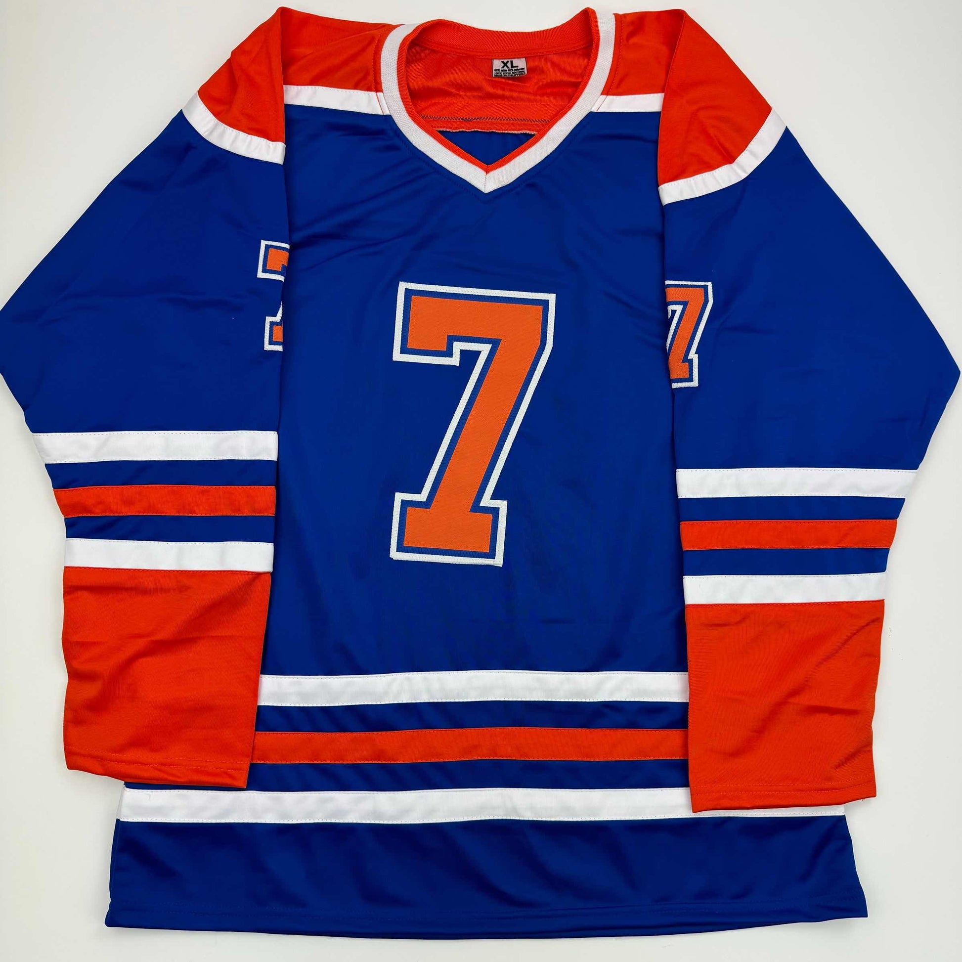 Blue Edmonton Oilers hockey jersey with orange number 7, red and white striping, displayed flat against white background.