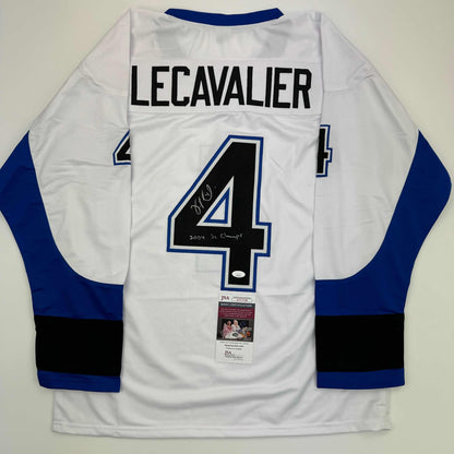 Back view of white hockey jersey with blue and black sleeves, number 4, "LECAVALIER" nameplate, autographed with "2004 SC Champs" inscription, and JSA certification label attached.
