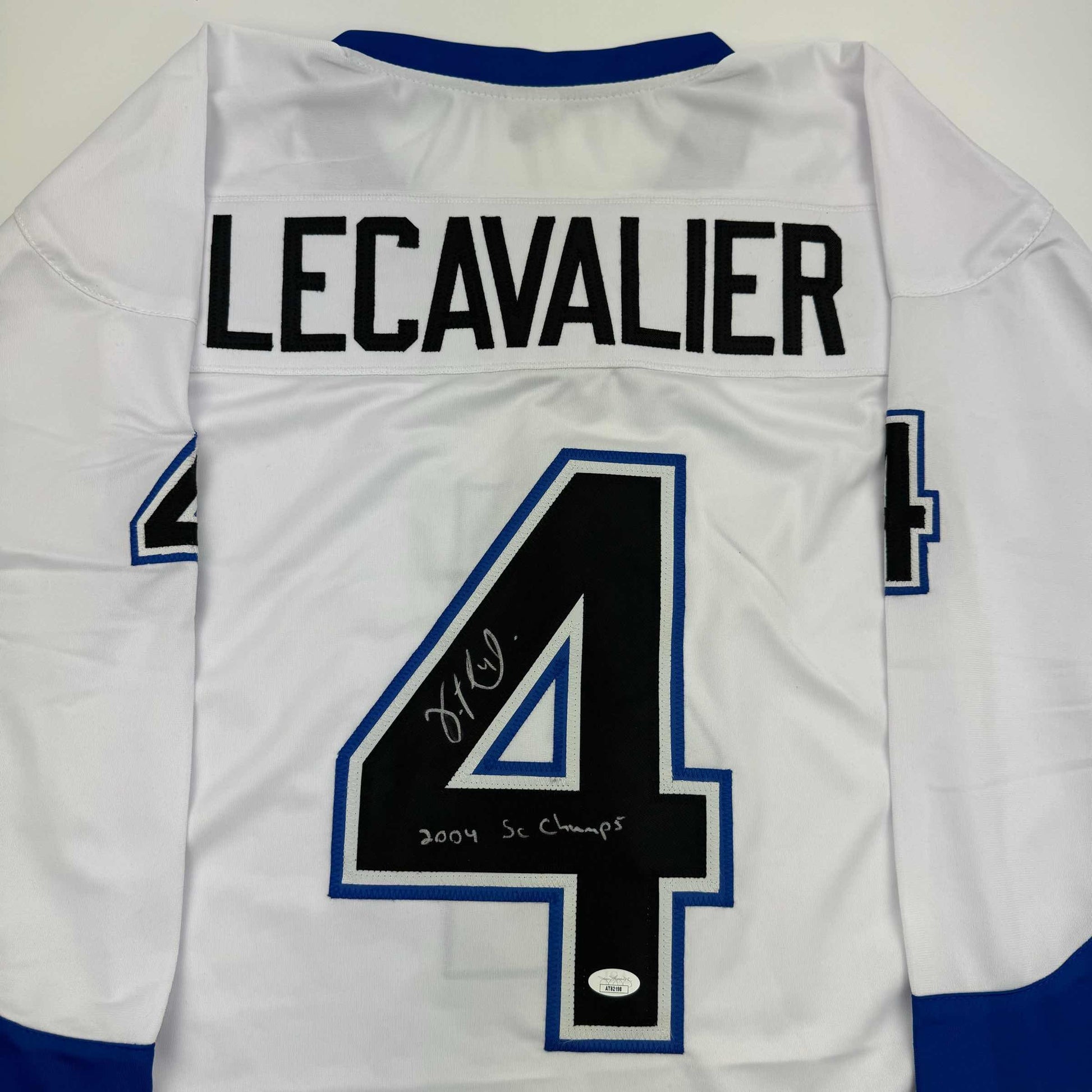 Back view of white hockey jersey with navy blue trim, displaying "LECAVALIER" across shoulders and large number 4, signed in black ink with "2004 SC Champs" notation.