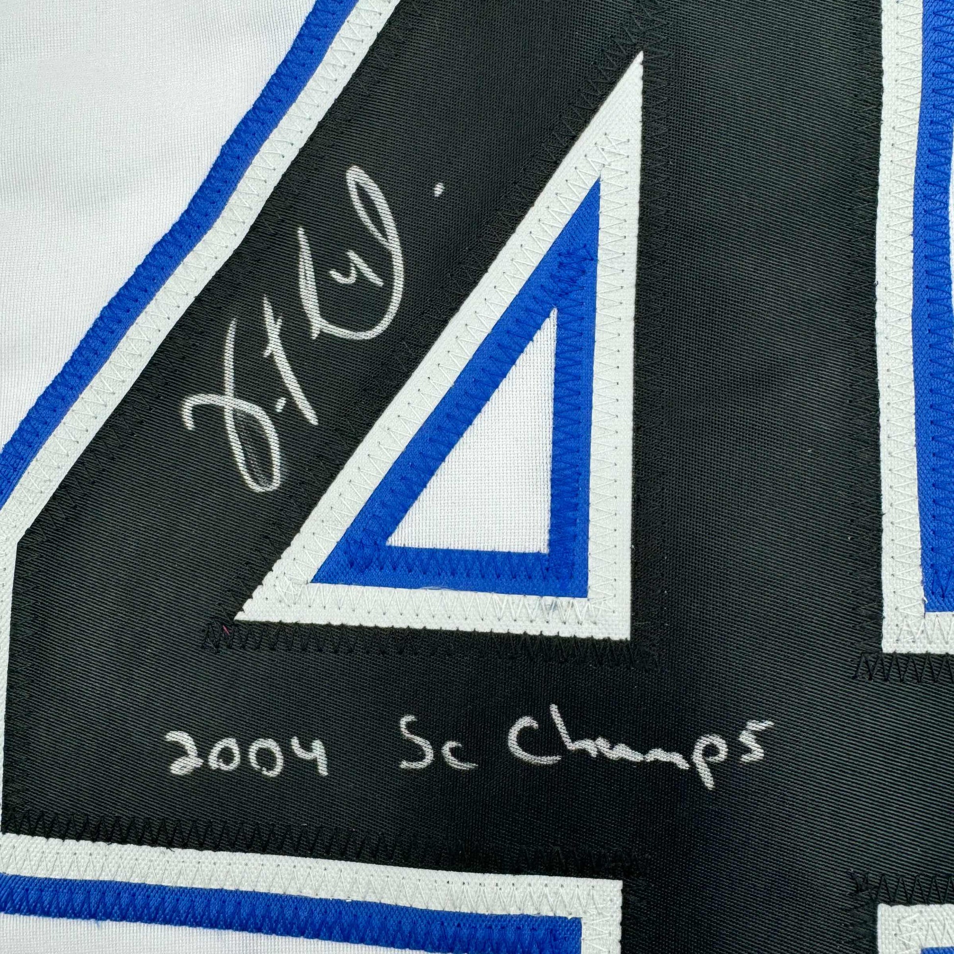 Close-up of autographed black jersey stripe showing handwritten signature and "2004 SC Champs" text with blue and white trim.