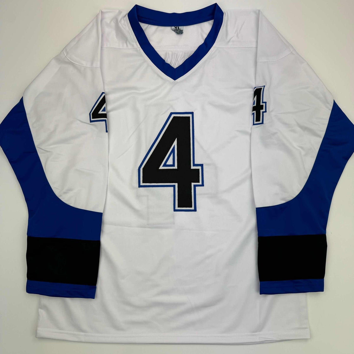 White hockey jersey with navy blue and black sleeves, large black number 4 with blue outline on chest, displayed flat against neutral background.
