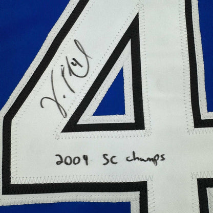 Close-up of autographed white hockey jersey stripe showing handwritten signature and "2004 SC champs" text on blue background.