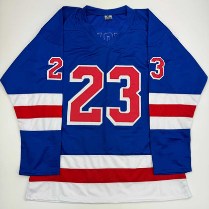 Blue New York Rangers hockey jersey with red number 23 displayed flat against white background, showing front view with striped sleeves.