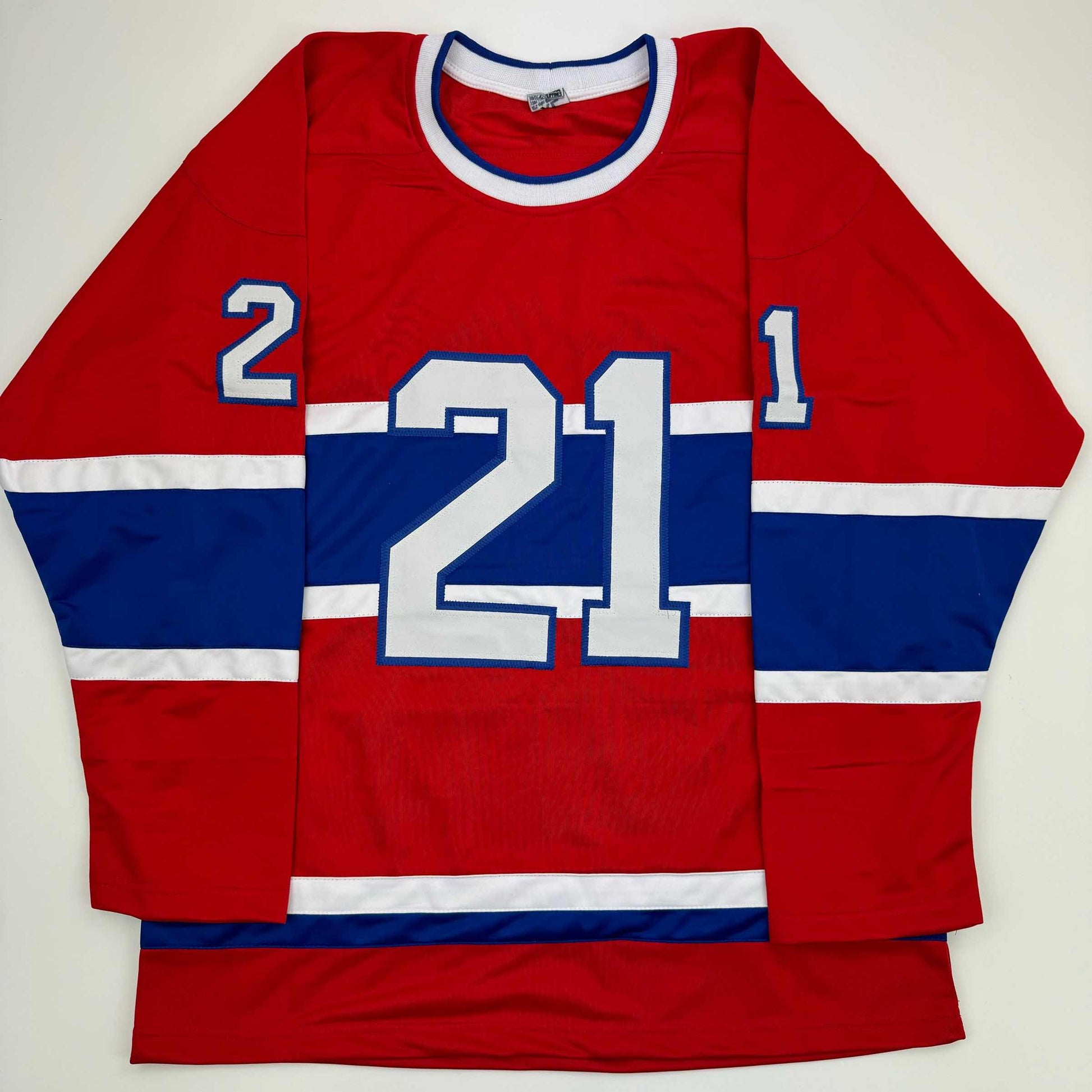 Red, white, and blue Montreal Canadiens hockey jersey with number 21 displayed flat against white background.