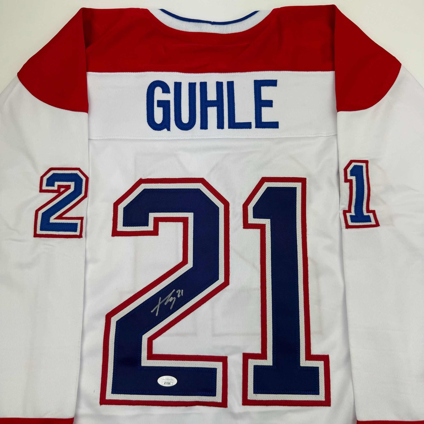Flat lay front view of white Montreal Canadiens hockey jersey with red sleeves, displaying "GUHLE" nameplate and number 21 with signature.