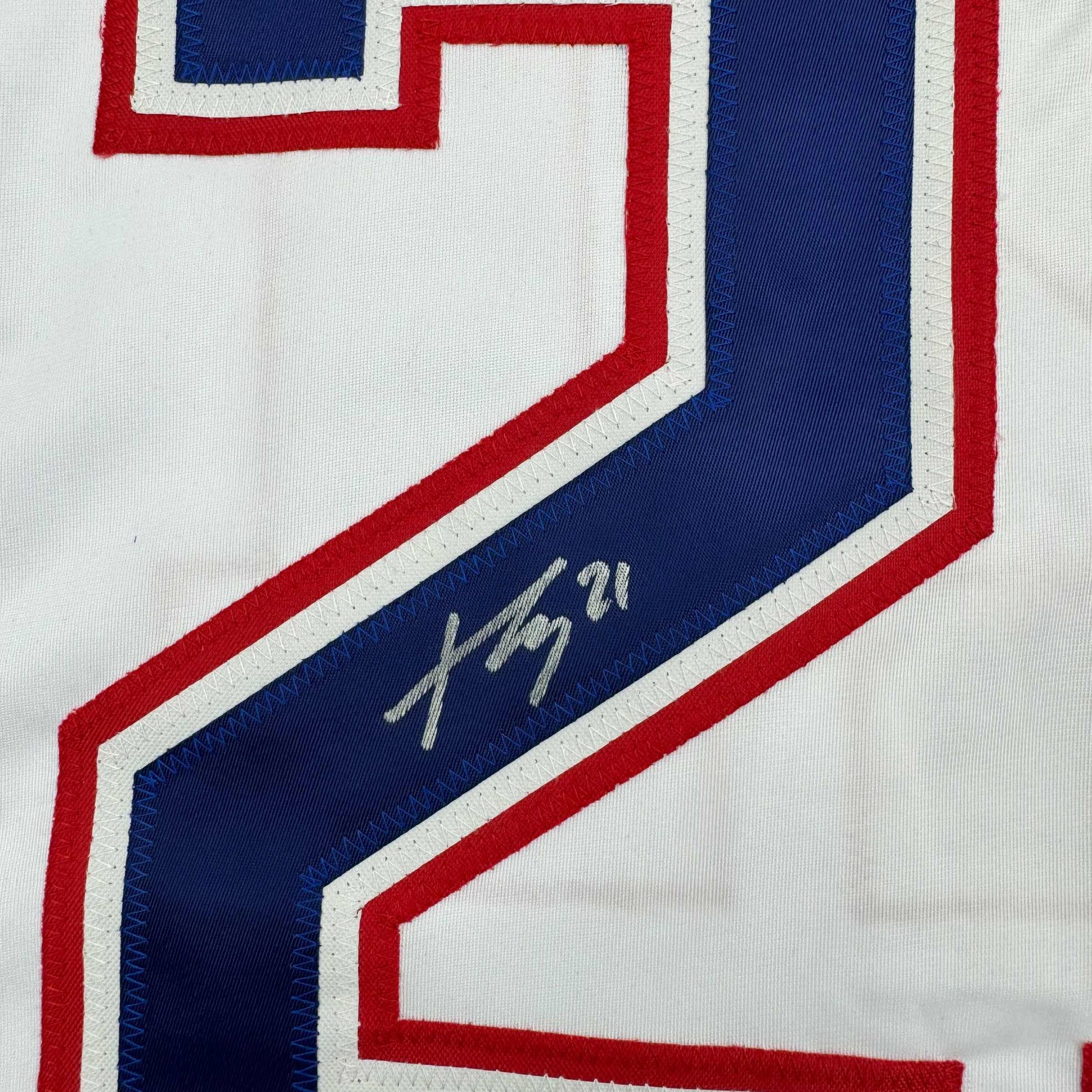 Close-up of signed blue stripe on white hockey jersey with red and white trim showing handwritten autograph.