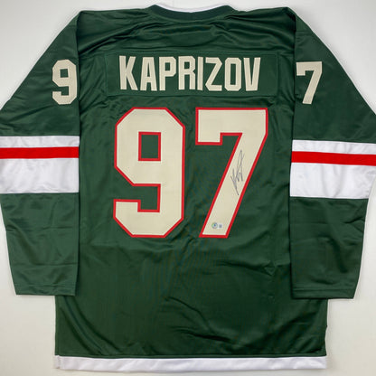 Back view of green hockey jersey with "KAPRIZOV" and number 97 in cream and red, displaying autograph signature on right side.