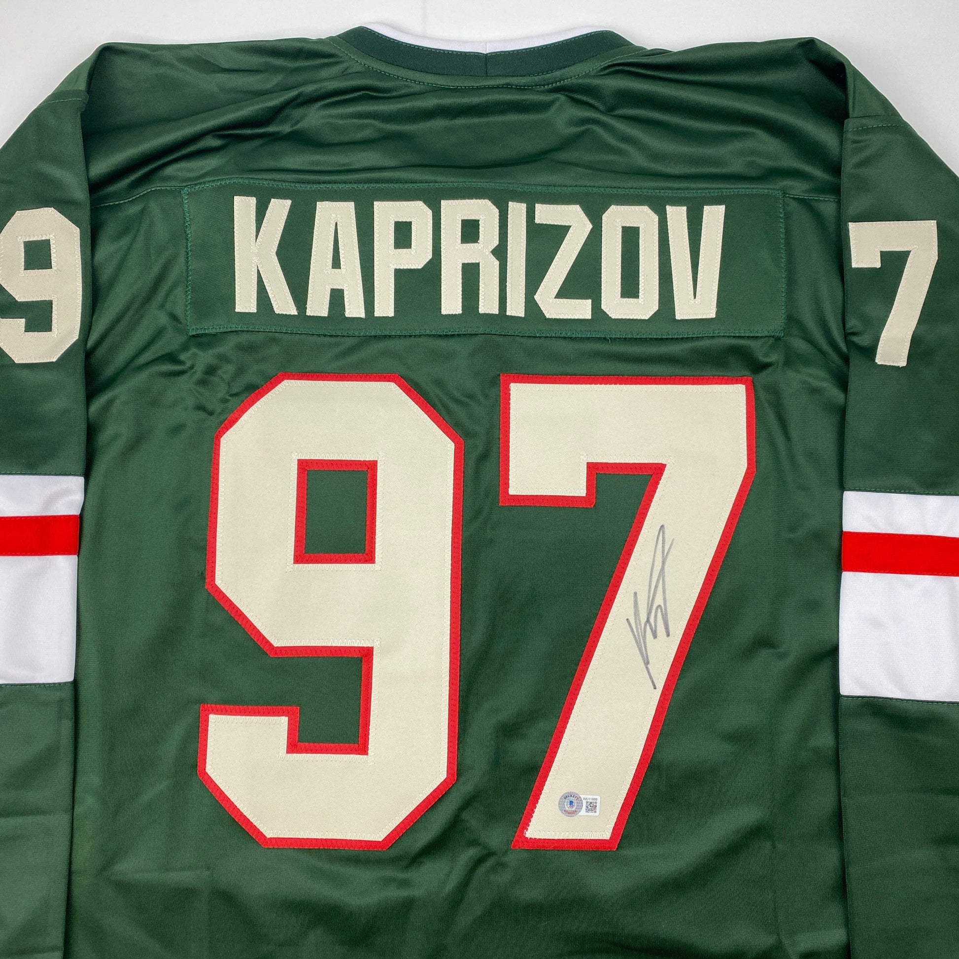 Back view of green hockey jersey displaying "KAPRIZOV" nameplate and numbers 9 and 7 in red and cream with signature.
