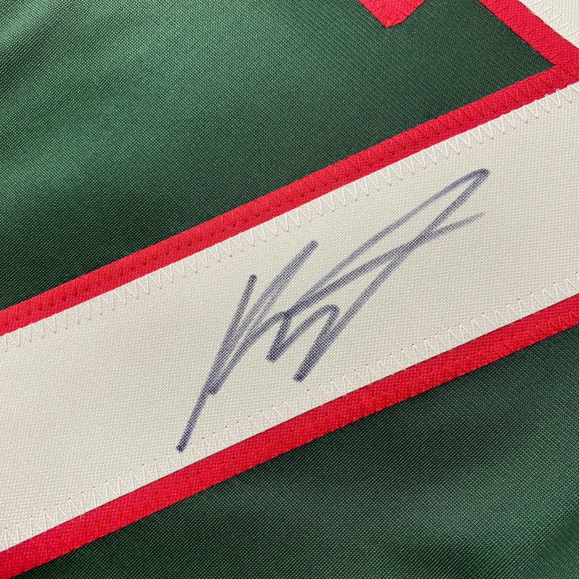 Close-up of blue handwritten signature on white stripe of green and red hockey jersey.