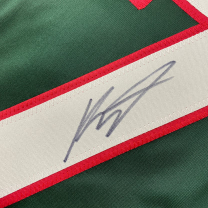Close-up of blue handwritten signature on white stripe of green and red hockey jersey.