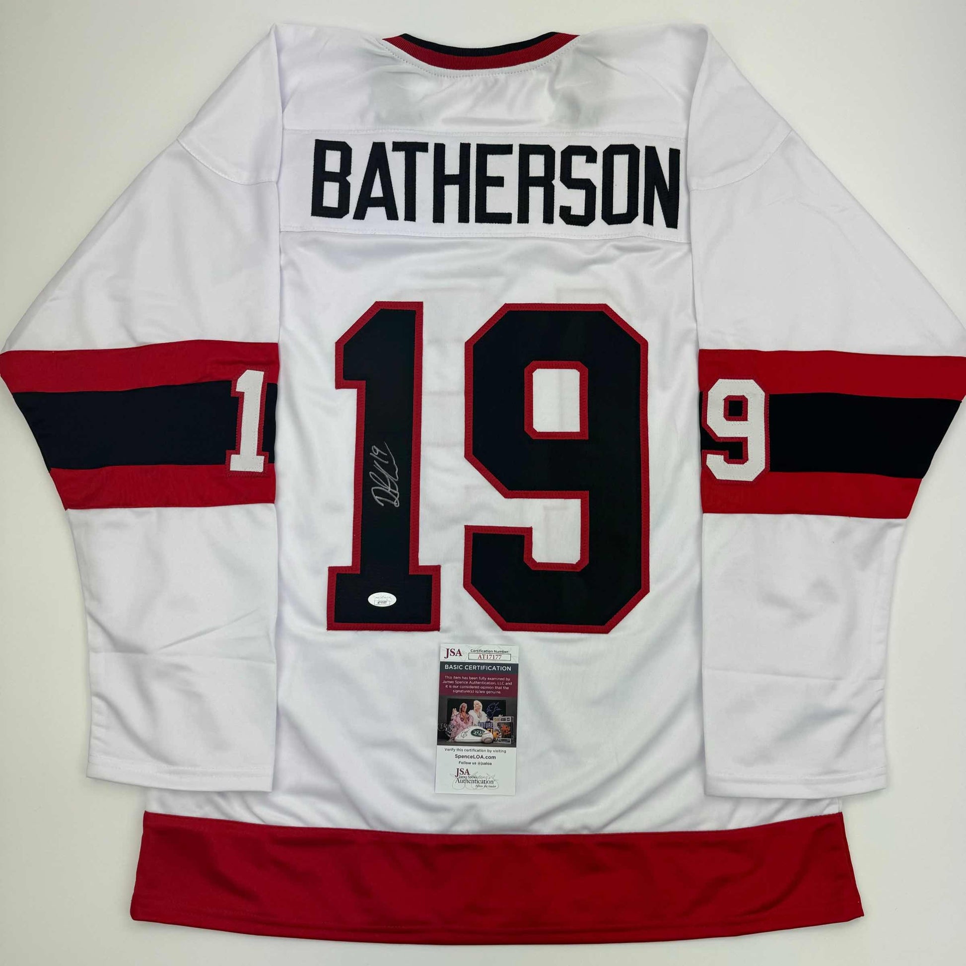 Back view of white hockey jersey with red and black striped sleeves, number 19, "BATHERSON" nameplate, and JSA authentication certificate visible.