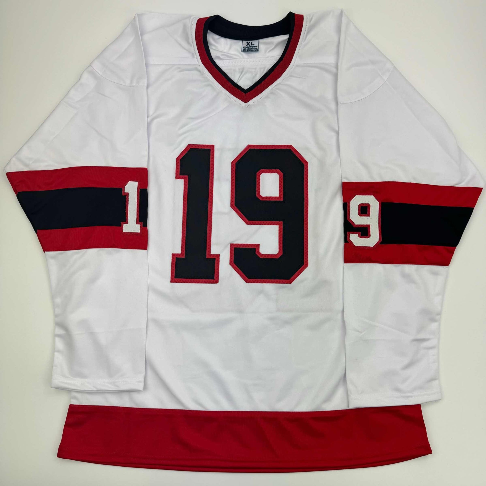 White hockey jersey with red and black striped sleeves, displaying black number 19 with red outline on chest, laid flat against white background.