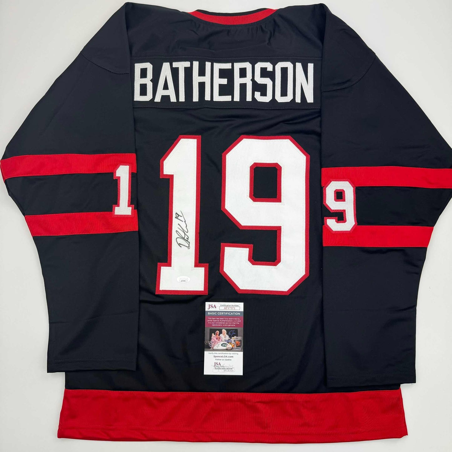 Back view of signed black and red striped hockey jersey with "BATHERSON" and number 19 in white and red lettering, with JSA authentication certificate attached.