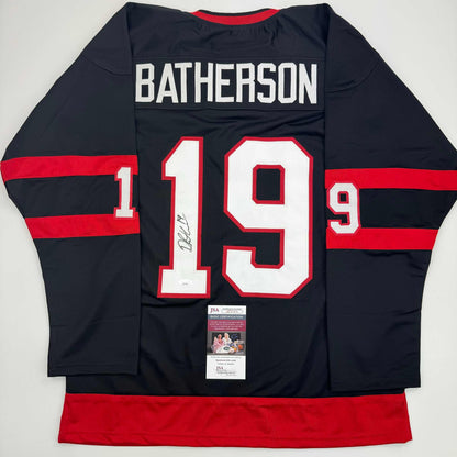 Back view of signed black and red striped hockey jersey with "BATHERSON" and number 19 in white and red lettering, with JSA authentication certificate attached.