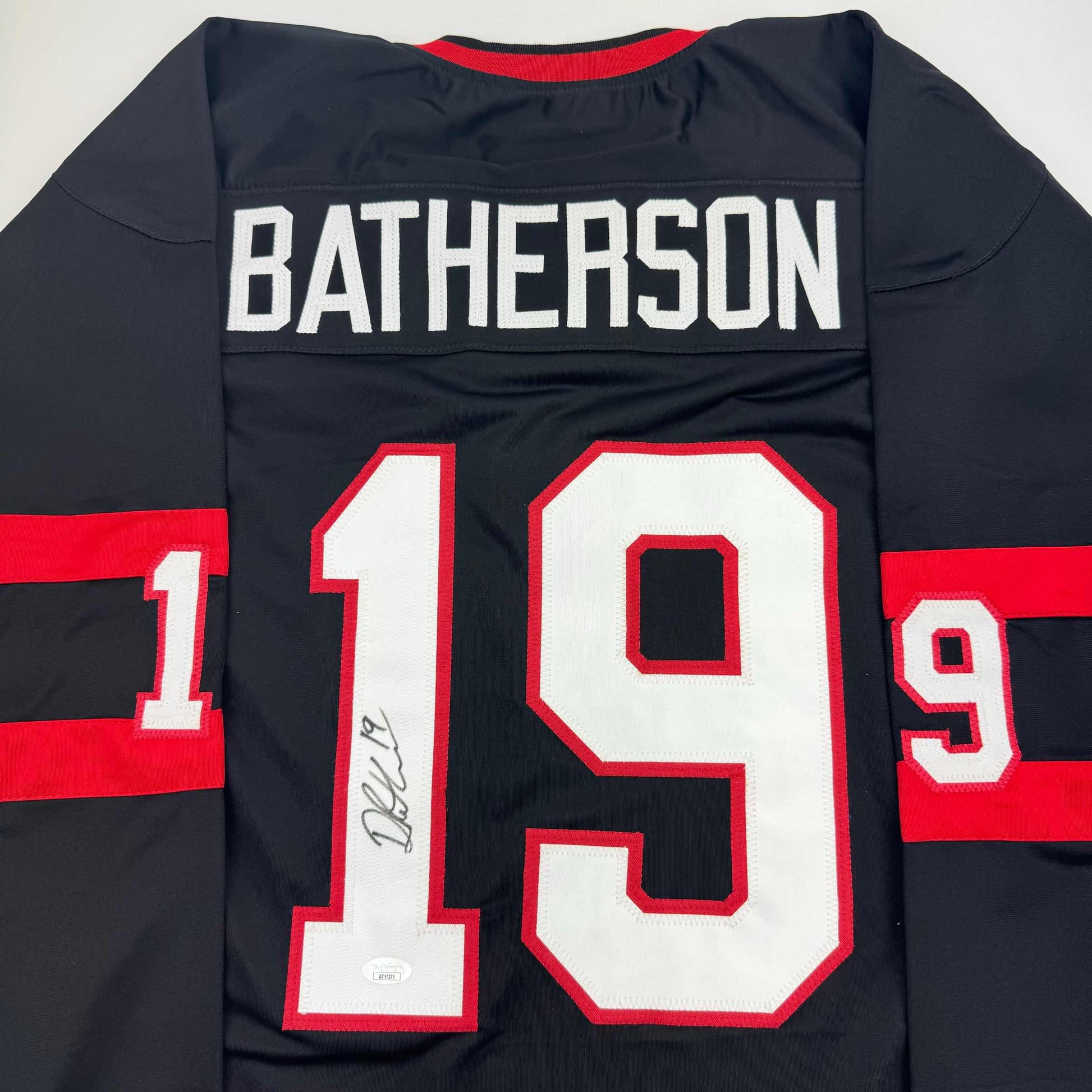 Back view of black and red striped hockey jersey with "BATHERSON" and number "19" in white lettering, signed in silver marker.