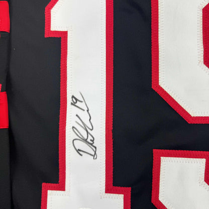Close-up of autographed white stripe on red and black striped hockey jersey showing handwritten signature.