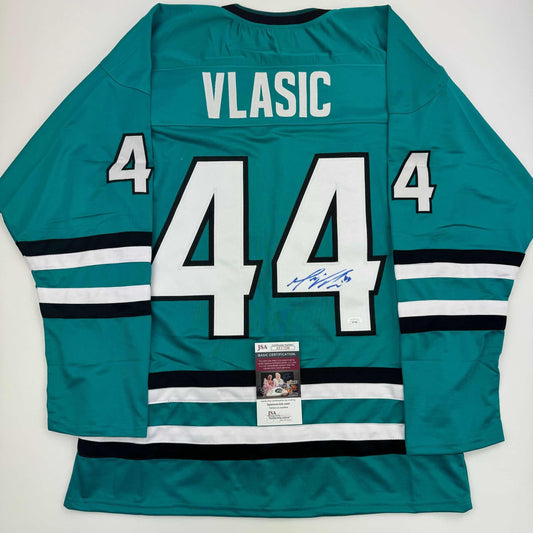 Rear view of teal San Jose Sharks hockey jersey number 44 with VLASIC name, displaying JSA authentication label and blue autograph on white number.