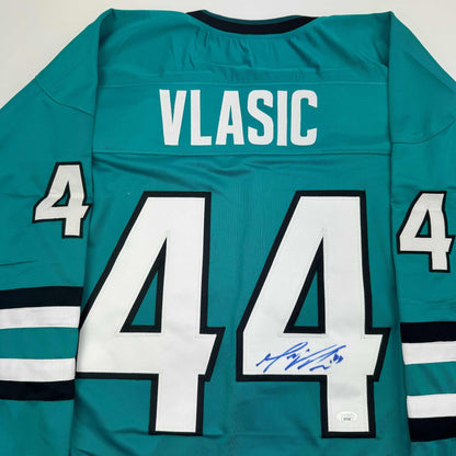 Teal San Jose Sharks hockey jersey displaying "VLASIC" and number 44 with blue autograph on back.