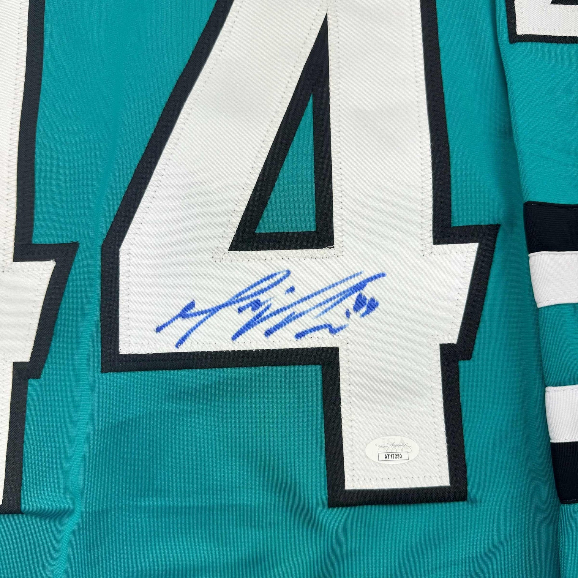 Close-up of signed teal and white hockey jersey showing blue autograph on white chest panel with black trim and JSA authentication label.
