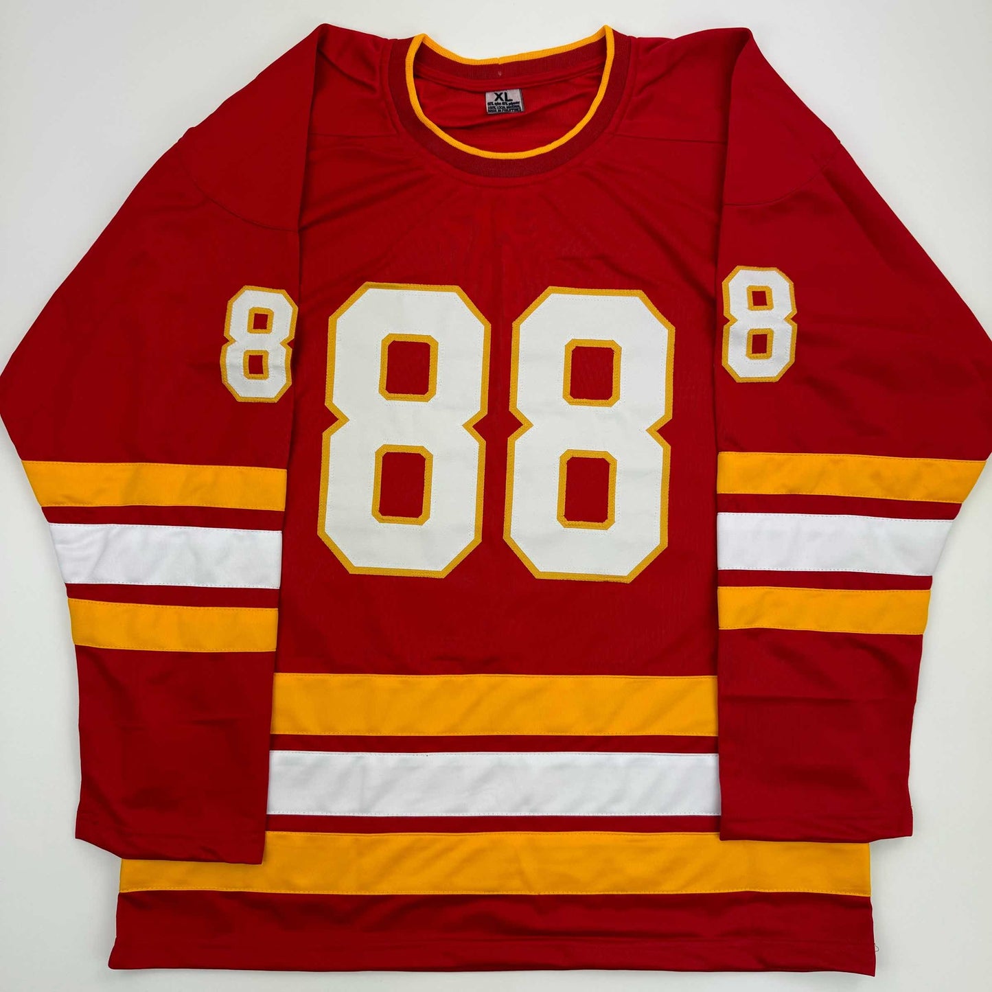 Red hockey jersey with white and gold number 88 displayed flat against white background, showing front view with striped sleeves.