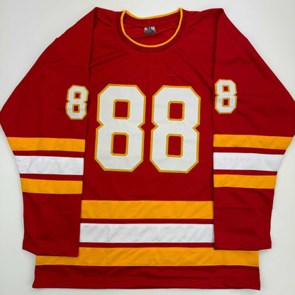 Red hockey jersey with white and gold number 88 displayed flat against white background, showing front view with striped sleeves.