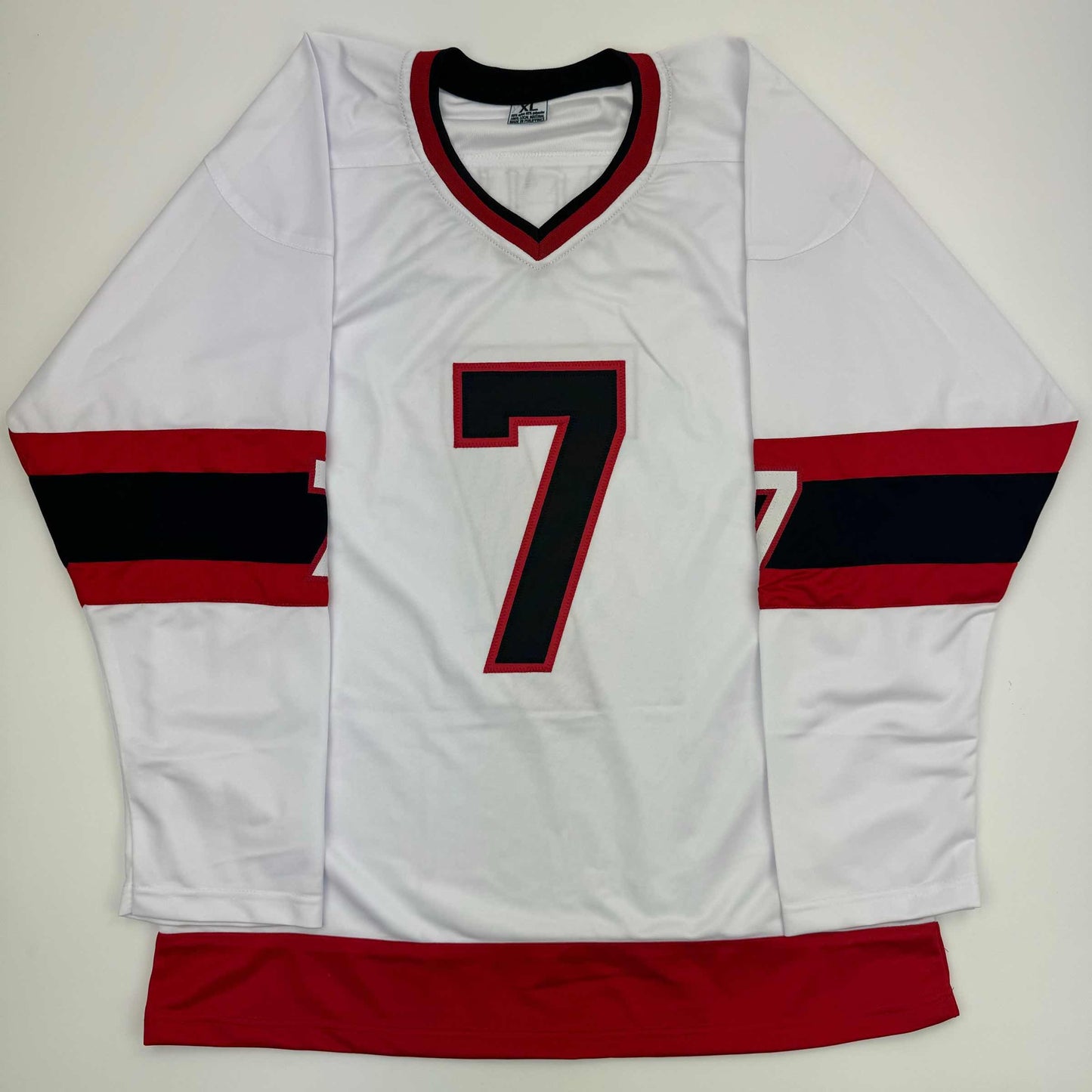 White hockey jersey with red and black horizontal stripes on sleeves, red V-neckline, and black number 7 on chest, displayed flat from front.