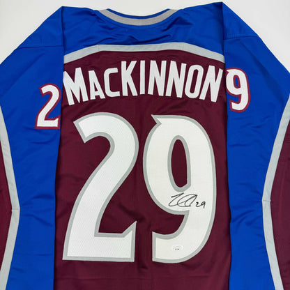Back view of maroon and blue Colorado hockey jersey with "MACKINNON 29" and autographed number 29 in white.
