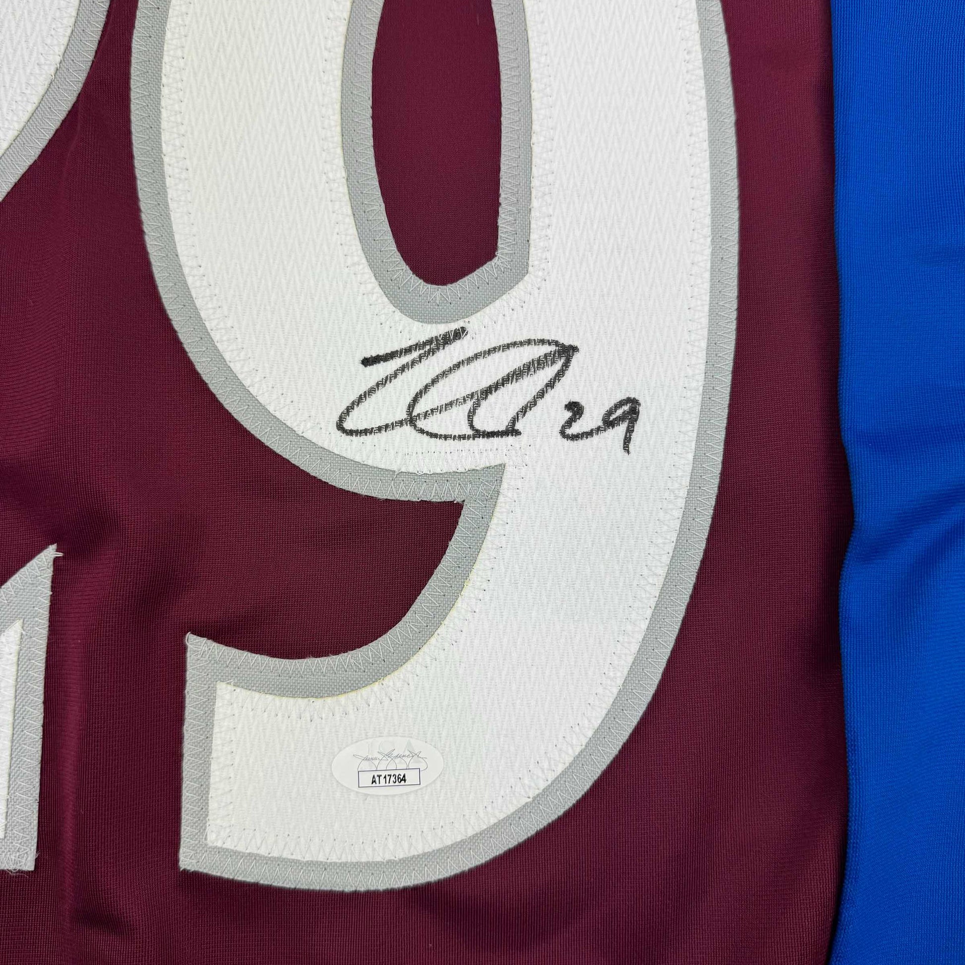 Close-up of signed maroon and white hockey jersey showing number 9 with handwritten autograph and JSA authentication sticker.