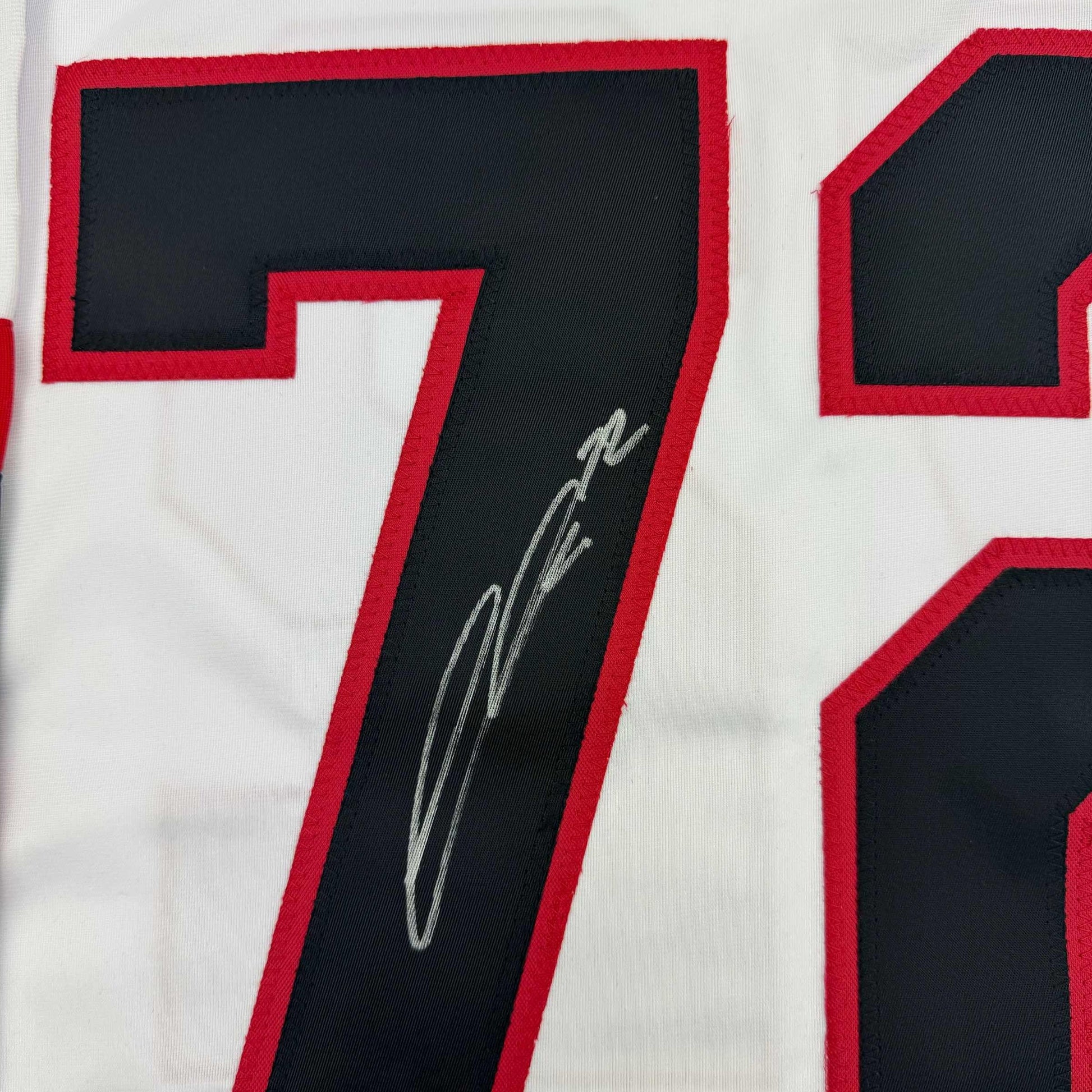 Close-up of number 7 on white hockey jersey with red trim, showing silver autograph signature on black fabric insert.