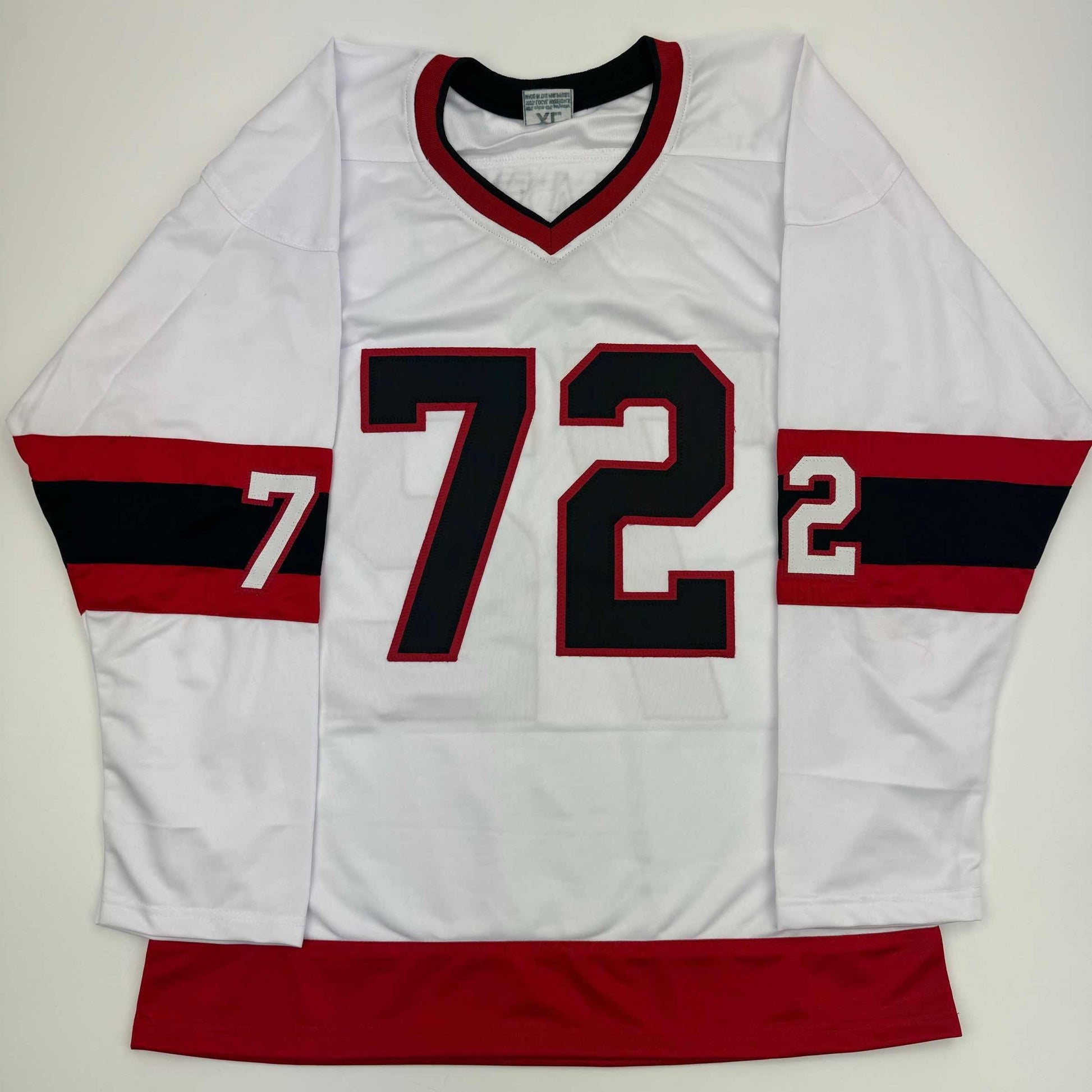White hockey jersey with red and black horizontal stripes on sleeves, displaying number 72 in black with red outline, laid flat on gray background.