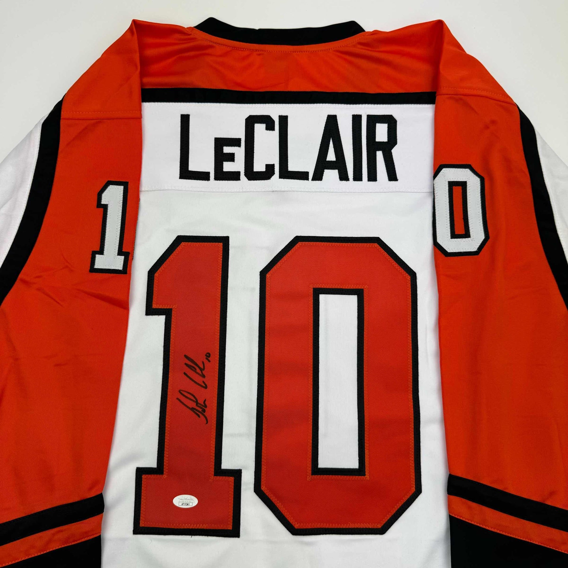 Back view of signed orange, white, and black hockey jersey displaying "LECLAIR" and number 10 with autograph on chest.