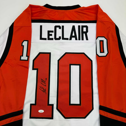 Back view of signed orange, white, and black hockey jersey displaying "LECLAIR" and number 10 with autograph on chest.
