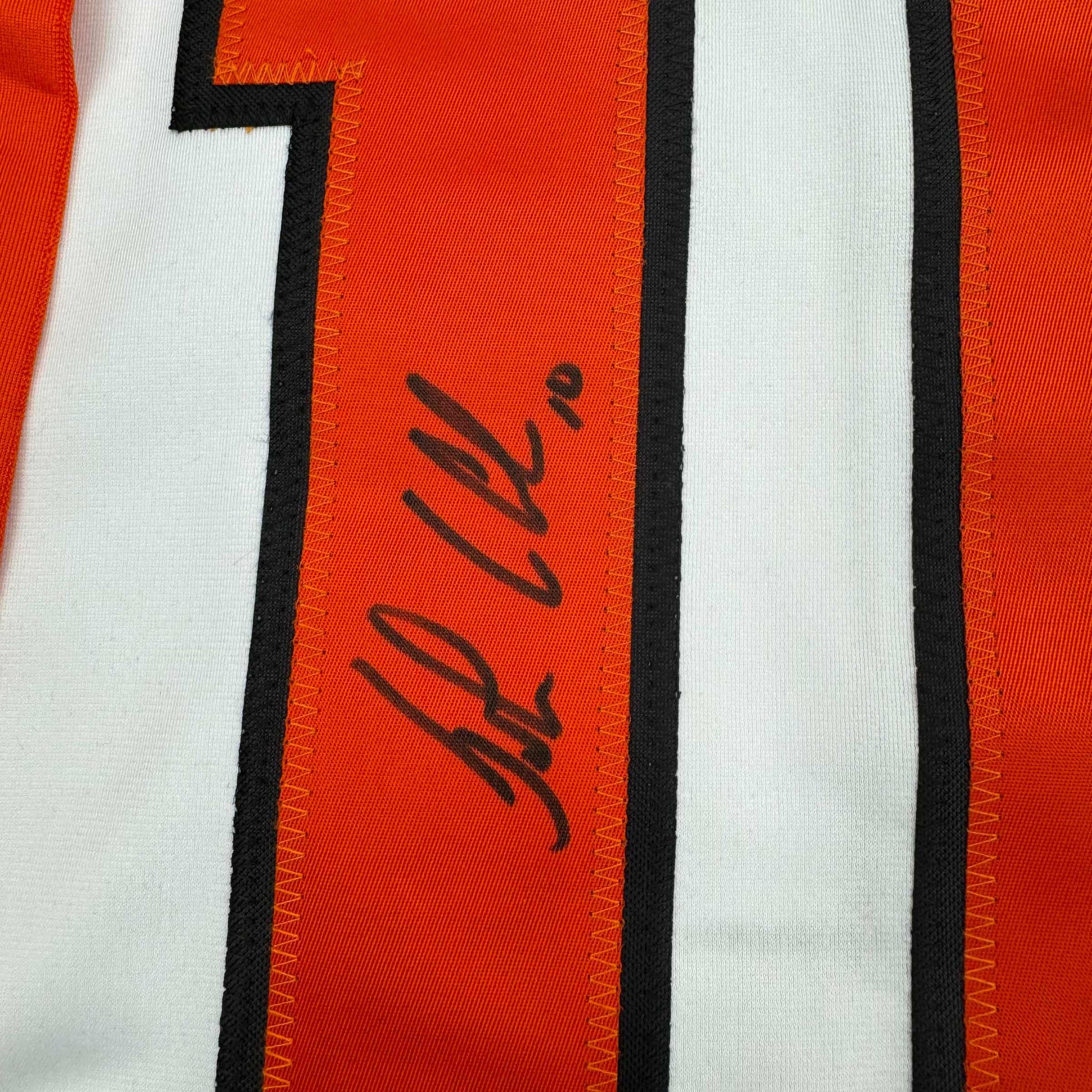 Close-up of autographed orange and white striped hockey jersey showing signed name on red central stripe.