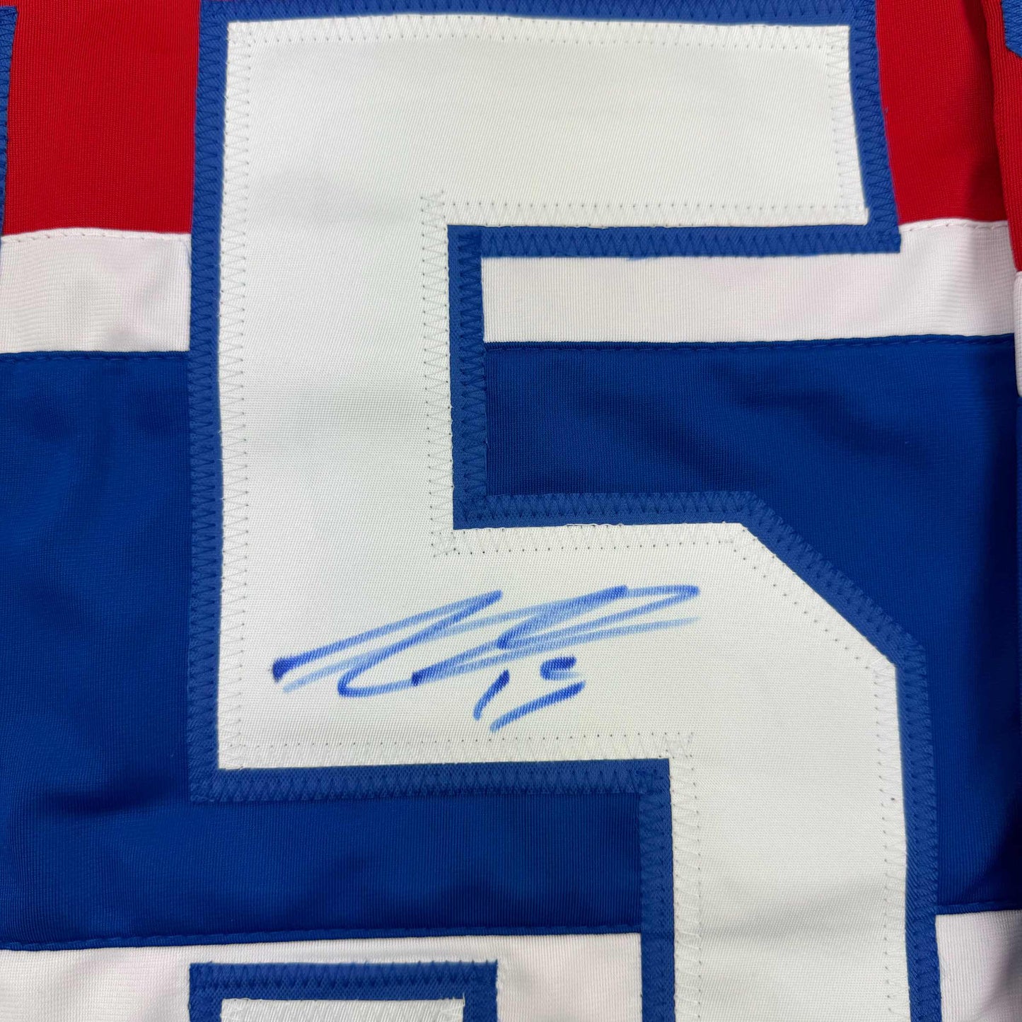Close-up of signed blue and white hockey jersey showing autographed number area with red and white striping.