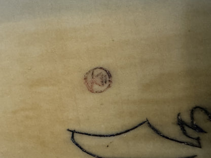 Close-up of carved ox horn pendant showing a smiling face with circular eyes and curved mouth line against cream-colored surface, detail view of Budai amulet.