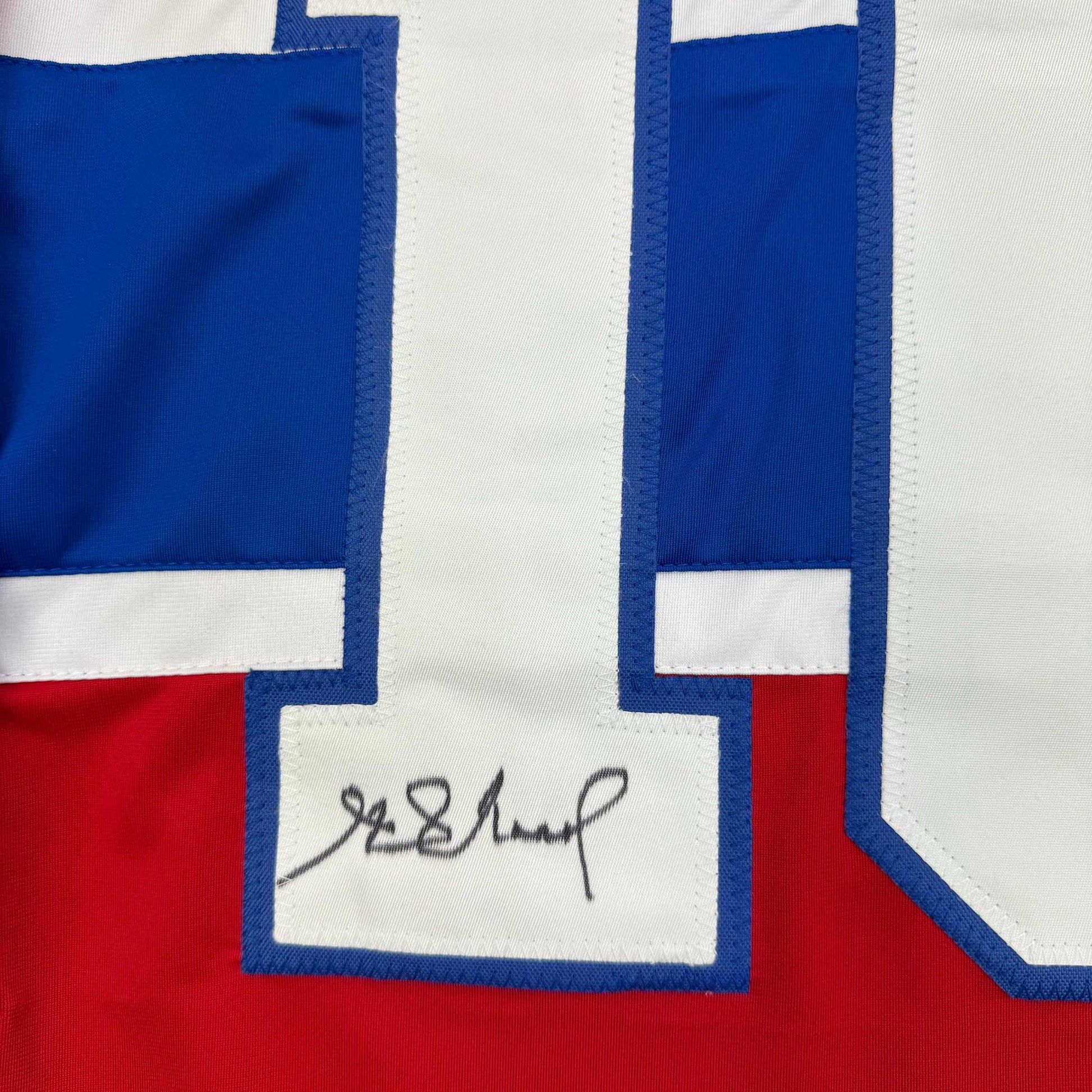 Close-up of handwritten signature on white panel of blue-bordered Montreal Canadiens hockey jersey with red and white sections.