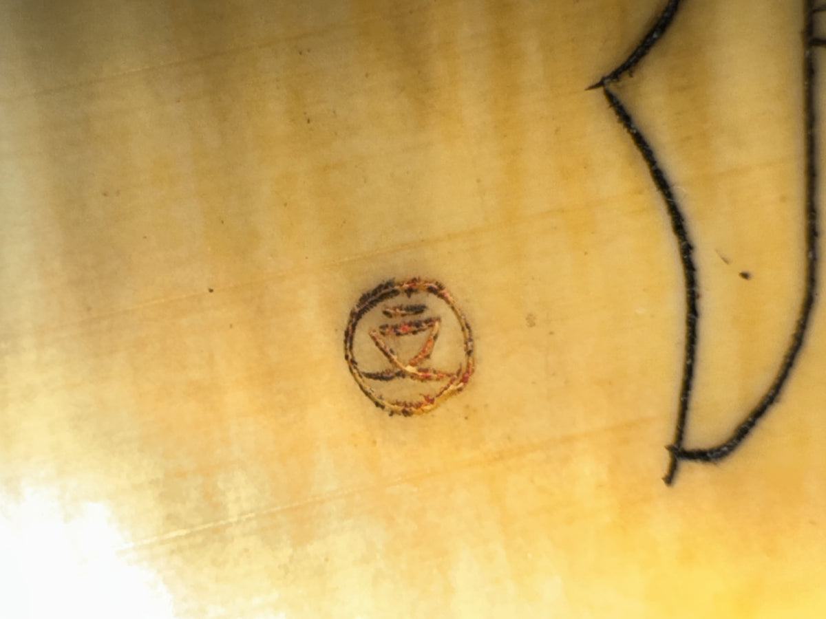 Close-up detail of carved ox horn pendant showing circular design with central figure and red/orange inlay, displayed on pale yellow fabric surface.